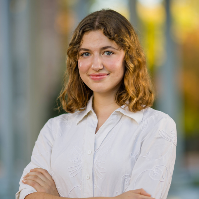 Abigail Schudel has arms crossed and stands in front of blurred background on the UNC campus.