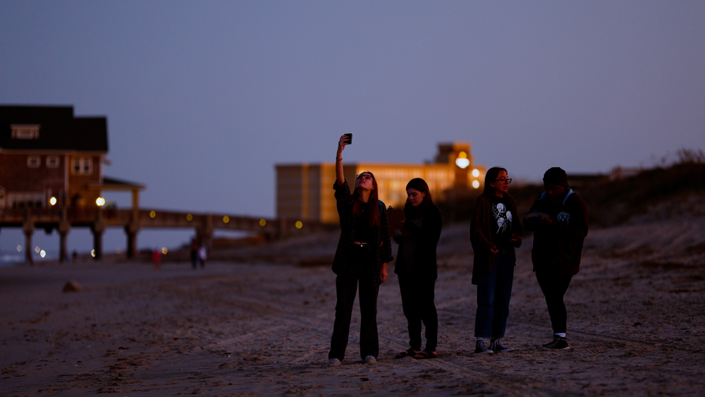 Students take light measurements on the beach at night.