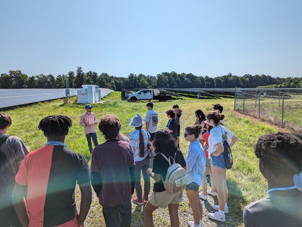 Students stand in front of solar panels on a field trip.